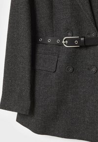 Blazer en laine chevrons gris foncé avec ceinture en cuir noire, détails de boutons et poche avant à rabat.