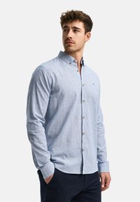 Camisa de botones a cuadros en azul claro con cuello extendido, mangas largas y botones marrones. La tela parece texturada y ligera.