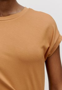T-shirt en coton marron avec un col rond et des manches courtes roulées. Texture lisse avec un léger stretch, mettant en valeur la douceur du tissu.