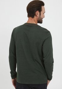 Langærmet skjorte i mørkegrøn bomuld med rund halsudskæring, prydet med orange stikninger langs kraven og skuldrene. Bagview.