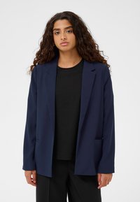 Navy zila žakete ar strukturētu dizainu, garām piedurknēm un brīvu piegriezumu, ar divām priekšējām kabatām un gludu auduma tekstūru.