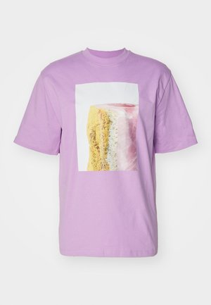 T-shirt en coton lilas avec une impression rectangulaire de dessert comportant des couches roses, jaunes et blanches. Manches courtes et col ras du cou.