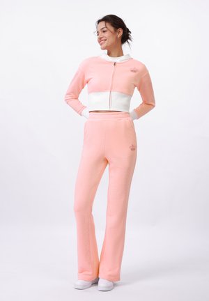 Sweatshirt cropped rose à fermeture éclair avec col blanc et pantalon de survêtement rose, tous deux en tissu doux, avec un détail de broderie en forme de couronne.