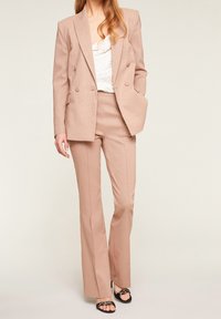 Blazer doppiopetto sagomato color rosa pallido e pantaloni a palazzo abbinati, realizzati in tessuto testurizzato, con tasche laterali e una silhouette elegante.