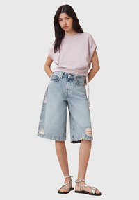 Maglietta corta di colore viola chiaro abbinata a pantaloni shorts in denim azzurro morbidi con bordi sfrangiati e dettagli strappati. Indossati con sandali argentati.