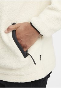 Fleecejack met een crèmekleurige, gestructureerde oppervlakte, voorzien van een zak met rits en zwarte rand, en een aansluitende boord.