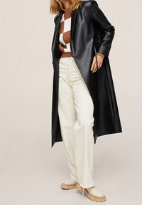 Sort læder lang frakke parret med en brun- og hvidstribet sweater, off-white jeans og beige platform sko. Glat tekstur, skræddersyet design.