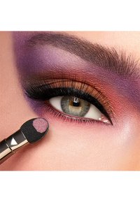 Application de maquillage mettant en avant un gros plan d'un œil avec un fard à paupières violet et orange. Un applicateur à embout en mousse avec un fard rose est utilisé.