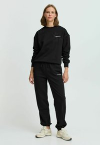 Sæt bestående af sort sweatshirt og sweatpants lavet af blødt stof, med en afslappet pasform, ribbede manchetter og logo-detaljer på begge dele.