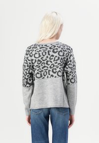 Un pull gris avec un motif léopard dans le haut du dos, texture en tricot, coupe décontractée et manches longues. Associé à un jean bleu.