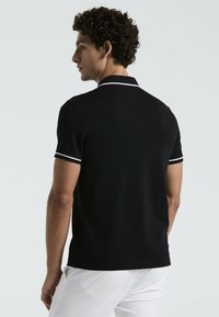 Schwarzes Poloshirt aus glattem Stoff, mit weißen Akzenten an Kragen und ärmelenden. Klassisches Design mit kurzen Ärmeln.