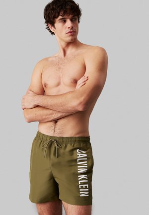 Pantaloni da bagno verde oliva con vita elasticizzata, cordoncino e logo bianco "CALVIN KLEIN" di lato. Tessuto dalla superficie liscia.