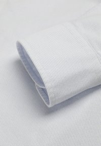 Primer plano de un puño de camisa de vestir azul claro con tela de textura fina y un sutil patrón de puntos azul oscuro.