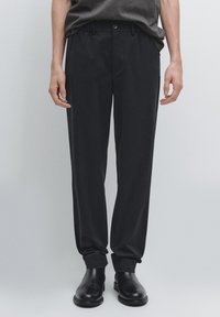 Pantalon noir à texture lisse, coupe droite et design classique avec une fermeture à bouton à l'avant et des poches latérales.