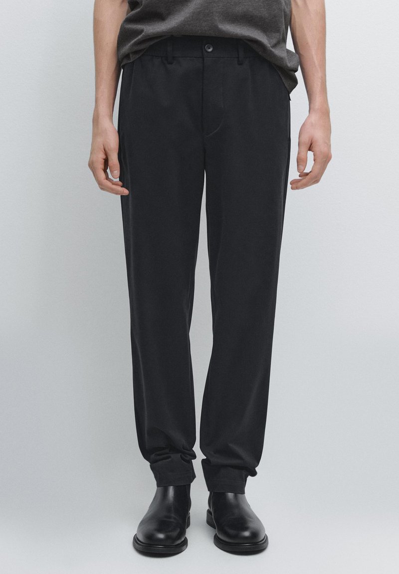 Pantalon noir à texture lisse, coupe droite et design classique avec une fermeture à bouton à l'avant et des poches latérales.