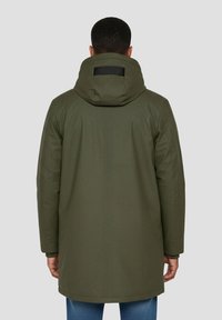 Parka verde oliva con textura acolchada, cuello alto y capucha desmontable. Cuenta con un pequeño detalle negro de velcro en la parte trasera.