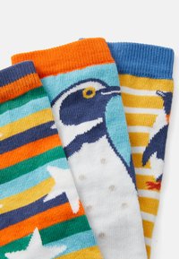 Drei Paar Baumwollsocken: eine mit einem Pinguin-Design, eine mit bunten Streifen und eine mit Sternmustern, alle in lebhaften Farben.