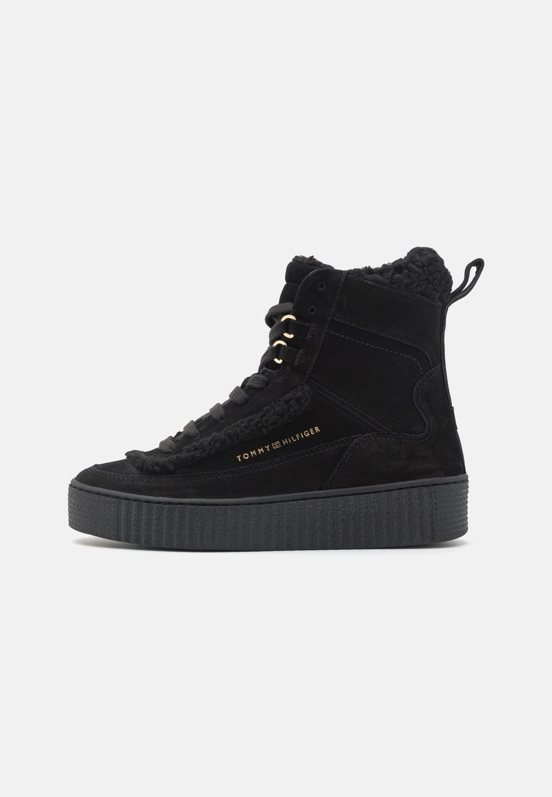 Baskets montantes noires avec semelle épaisse, lacets à l'avant, doublure en polaire, et logo "Tommy Hilfiger" doré sur le côté.