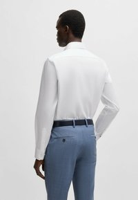 Witte longsleeve blouse met een klassieke kraag; gecombineerd met lichtblauwe textuur broek en een donkeren blauwe riem. Knopen zijn zichtbaar op de mouwen.