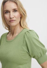 Grøn strikbluse med rund halsudskæring, korte puffærmer med ribbede manchetter og en glat, let tekstur.