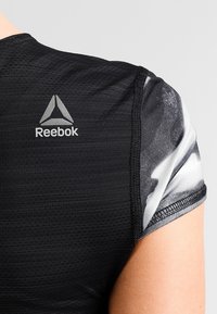 Svart träningsskjorta med textilstruktur, har kort ärm i ett grått och vitt abstrakt mönster, logotyp på ryggen i grått.