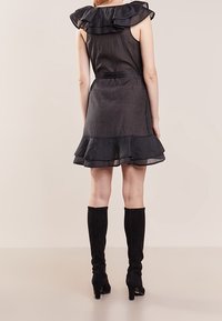 Musta hihaton mekko, jossa on röyhelöilystä kaula-aukko ja helma, valmistettu kevyestä kankaasta. Yhdistetty polvipitkiin mustiin mokkasaappaisiin.