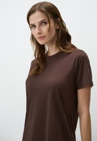 Bruin T-shirt met korte mouwen van zachte, gladde stof met een ronde hals. Eenvoudig ontwerp, aansluitende silhoutte en minimale stikseldetails.