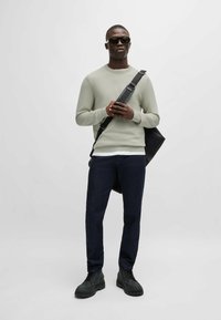 Lichtgroene trui, donkere jeans, zwarte laarzen, zonnebril en een zwarte schoudertas. Getextureerde stof, casual pasvorm, modern ontwerp.