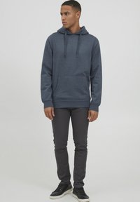 Donkerblauwe hoodie van een katoenmix, met een voorkantzak, verstelbare koordjes en geribbelde manchetten. Gecombineerd met donkergrijze broeken en zwarte sneakers.