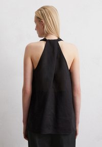 Un haut sans manches noir avec un col montant, fabriqué en tissu léger. Doté d'un dos drapé et d'une texture lisse. Conception simple sans motifs.