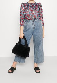 Black faux fur handbag with two short handles, paired with a floral patterned top and wide-leg blue denim jeans. Black flat slides worn.