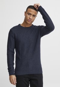 Pulover tricotat bleumarin cu guler rotund, manșete și margine cu nervuri. Prezintă un model texturat cu un design aproape ajustat.