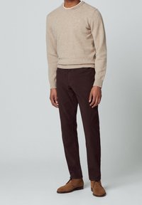 Maglione lavorato a maglia beige con scollo rotondo, abbinato a chinos marrone scuro e stivaletti alla caviglia in camoscio marroni. Design semplice, texture morbida.