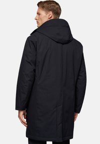 Abrigo negro con capucha de corte recto, con mangas largas y una textura suave y mate. Sin herrajes visibles ni patrones.