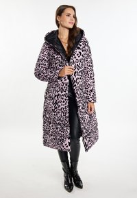 Gepolsterter Mantel in Hellrosa mit schwarzem Leopardenmuster, ausgestattet mit einer Kapuze und einem Reißverschluss. Glänzende schwarze kniehohe Stiefel runden das Outfit ab.