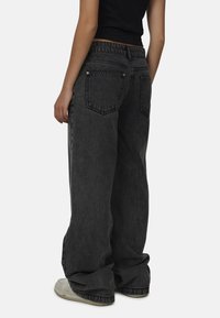 Czarne dżinsy typu wide-leg z wysokim stanem, z podwójnymi tylnymi kieszeniami i delikatnie wyblakłą fakturą, które zestawiono z jasnymi trampkami.