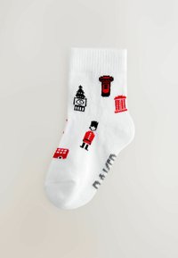 Chaussette blanche en coton à la cheville ornée d'icônes brodées en rouge et noir, comprenant un soldat, une boîte aux lettres et un bus. Texture douce, bord-côte.