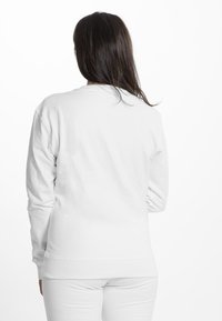 Vit crewneck sweatshirt med långa ärmar. Mjuk tyg, ribbade muddarna och rak fåll. Enkelt, minimalistisk design, inga synliga logotyper.