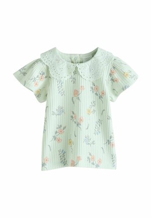 Haut vert clair motifé avec un col bordé de dentelle. Il présente des manches courtes à volants et des imprimés floraux en rose, bleu et jaune.