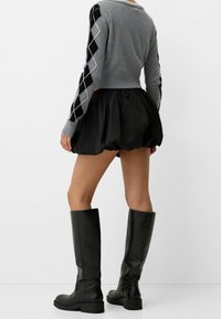 Grå tröja med långa ärmar som har ett svartvitt argyle-mönster, tillsammans med en svart puffig kjol och knähöga svarta stövlar.