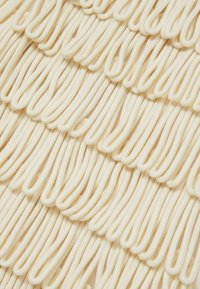 Tessuto di crema texturizzato con anse, creando un motivo ondulato. Fili morbidi e flessibili disposti in orizzontale, che aggiungono volume e profondità.