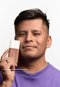 Butelka podkładu o matowym brązowym korpusie i białej pokrywce, oznaczona napisem "Głęboki chłodny". Osoba trzyma ją na tle białym.