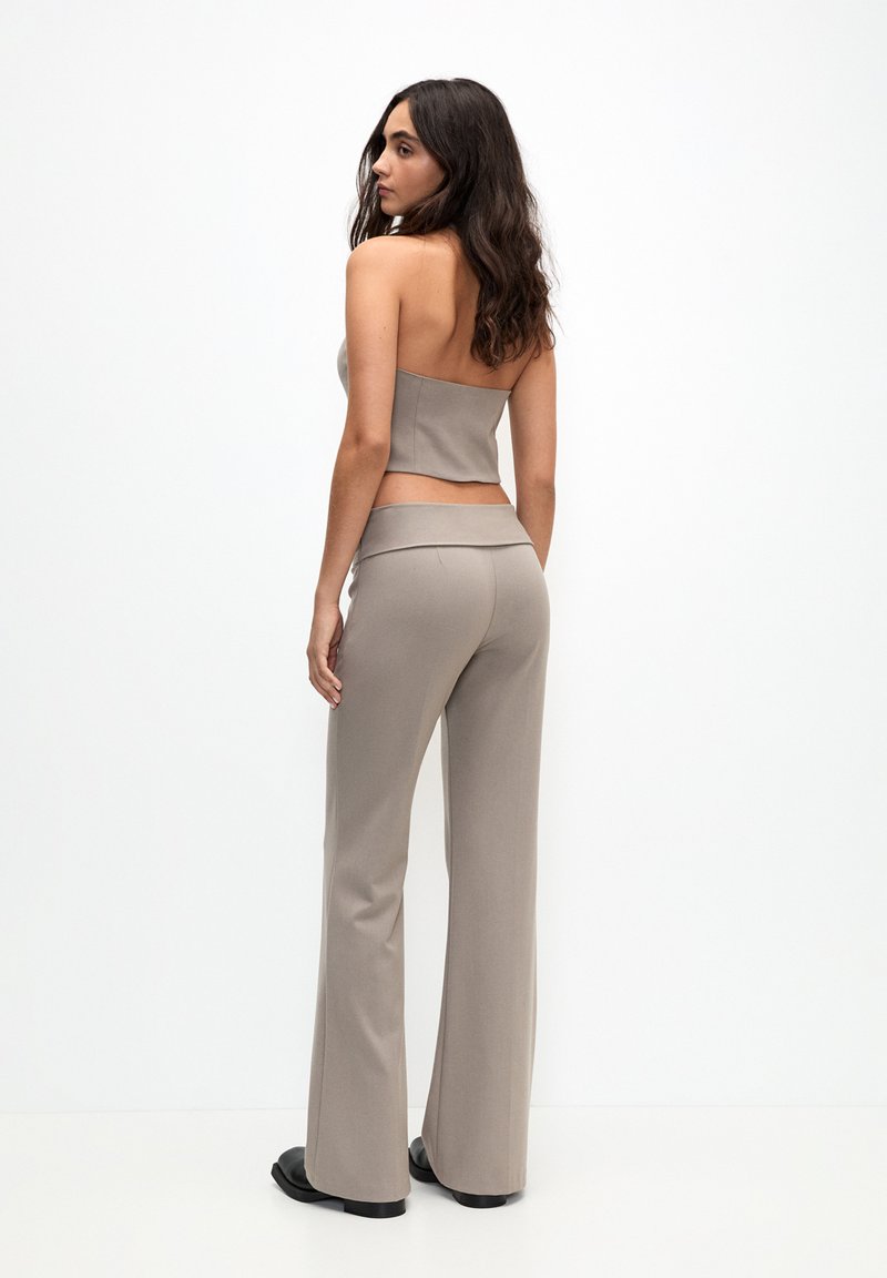 Hellbraunes Zweiteiler-Outfit mit einem taillierten, trägerlosen Oberteil und hochgeschnittenen, ausgestellten Hosen, gefertigt aus einem glatten, dehnbaren Stoff.