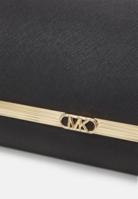 Must have musträbimustkott kuldse detailiga, millel on ristkülikuline logo. Tekstureeritud pind koos ribakujulise aksentvööndi keskel.