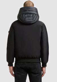 Chaqueta acolchada negra con capucha alta y acolchada, y puños de canalé. Presenta una textura suave y una silueta corta para un look moderno.