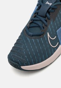 Scarpa sportiva con tomaia in mesh blu scuro, caratterizzata da una superficie testurizzata, dettagli contrastanti in blu chiaro e suola in gomma rosa.