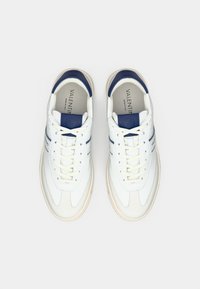 Bílé kožené tenisky s námořnicky modrými detaily, mají texturovaný svršek, kulatou špičku, šněrování vpředu a béžovou gumovou podrážku. Logo značky na jazyku.
