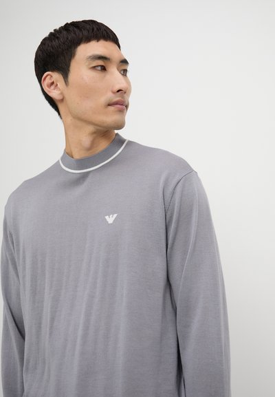 Maglione grigio con una finitura testurizzata, collo alto e bordi bianchi a contrasto. Presenta un piccolo logo bianco sul petto.