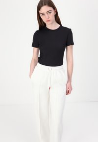 Camiseta negra de manga corta combinada con pantalones blancos que cuentan con una cintura ajustable y detalles en rojo. Diseño simple y ajustado con una textura suave.