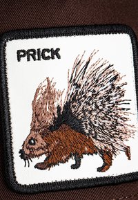 Patch ricamato con un istrice in filo marrone e nero su uno sfondo bianco, con la parola "PRICK" in testo nero.